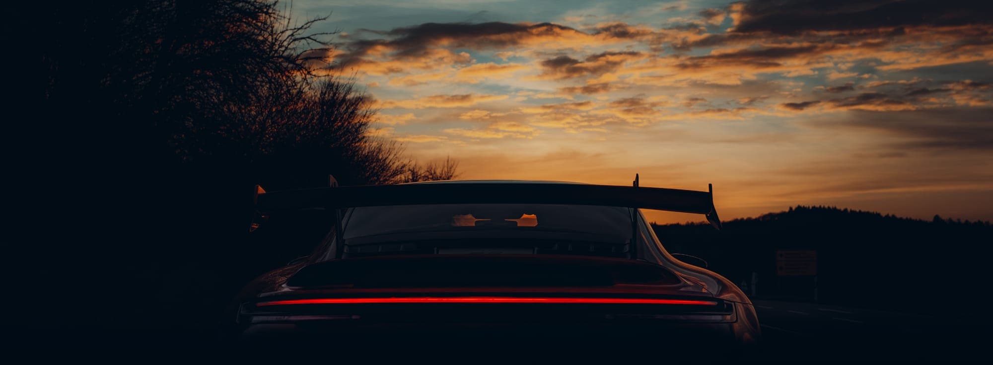 The rear wing of a Porsche 911 GT3 silhouetted against the evening sky.