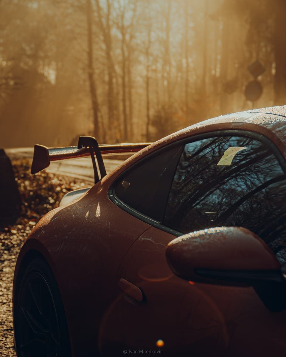 The rain-covered rear wing of a red Porsche 911 GT3 in autumn light.