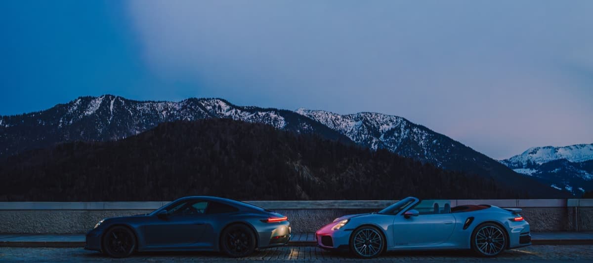 Two Porsche 911 Turbos beneath snow-covered Alpine peaks at blue hour.